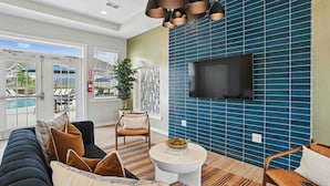 Un salon moderne avec un canapé, des fauteuils, une table basse et un téléviseur fixé au mur, qui est recouvert de carreaux bleus.