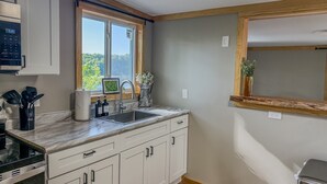 A kitchen with a built-in oven, a sink, and a window with a view of greenery. - Lookout Lodge | Waterfront | Private Dock (Hammond)