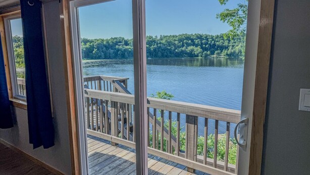 A room with a sliding glass door leading to a wooden deck overlooking a lake. - Lookout Lodge | Waterfront | Private Dock (Hammond)