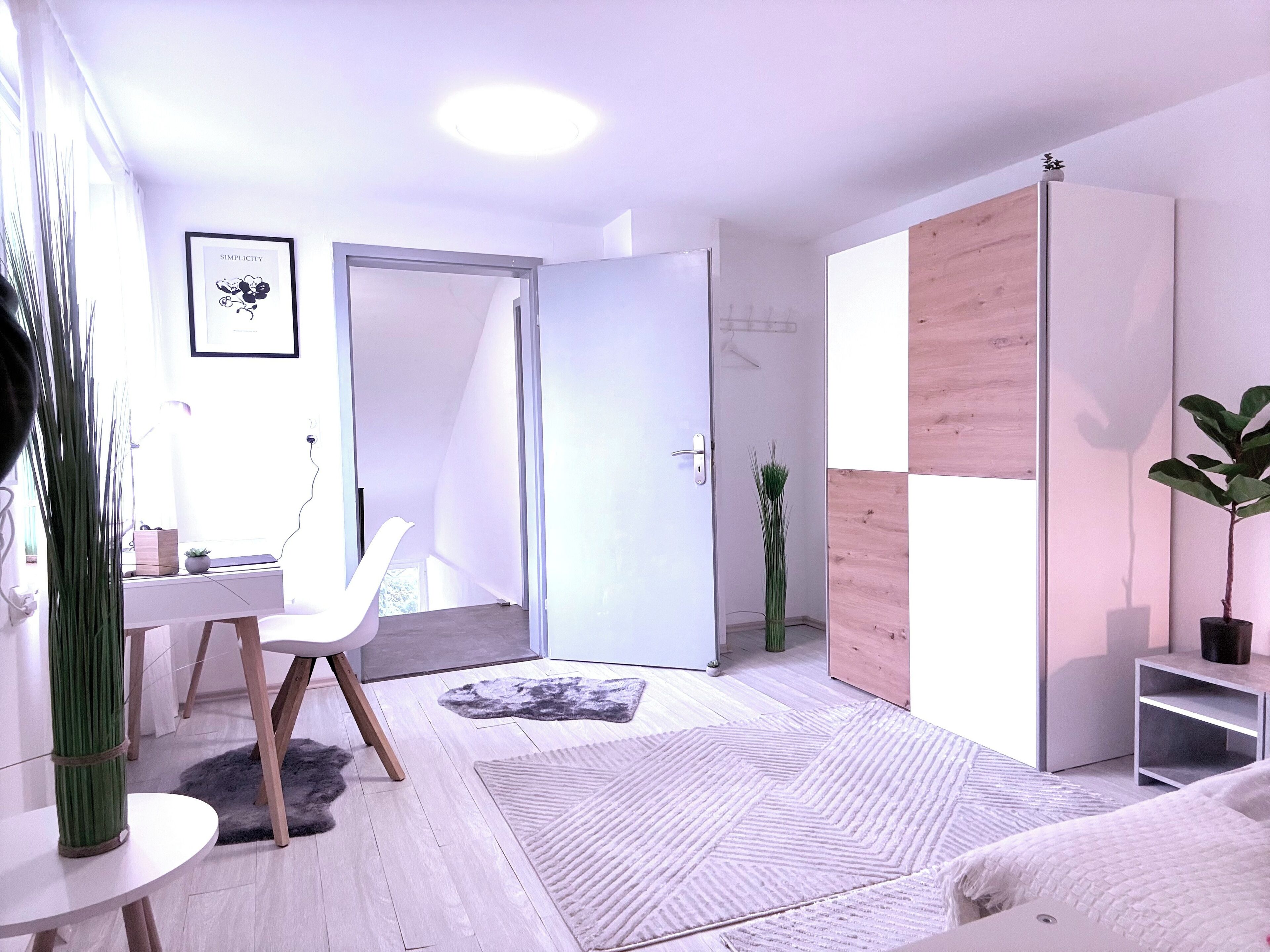 Une pièce moderne et bien éclairée, avec un bureau blanc, une chaise, une grande armoire et une plante en pot.
