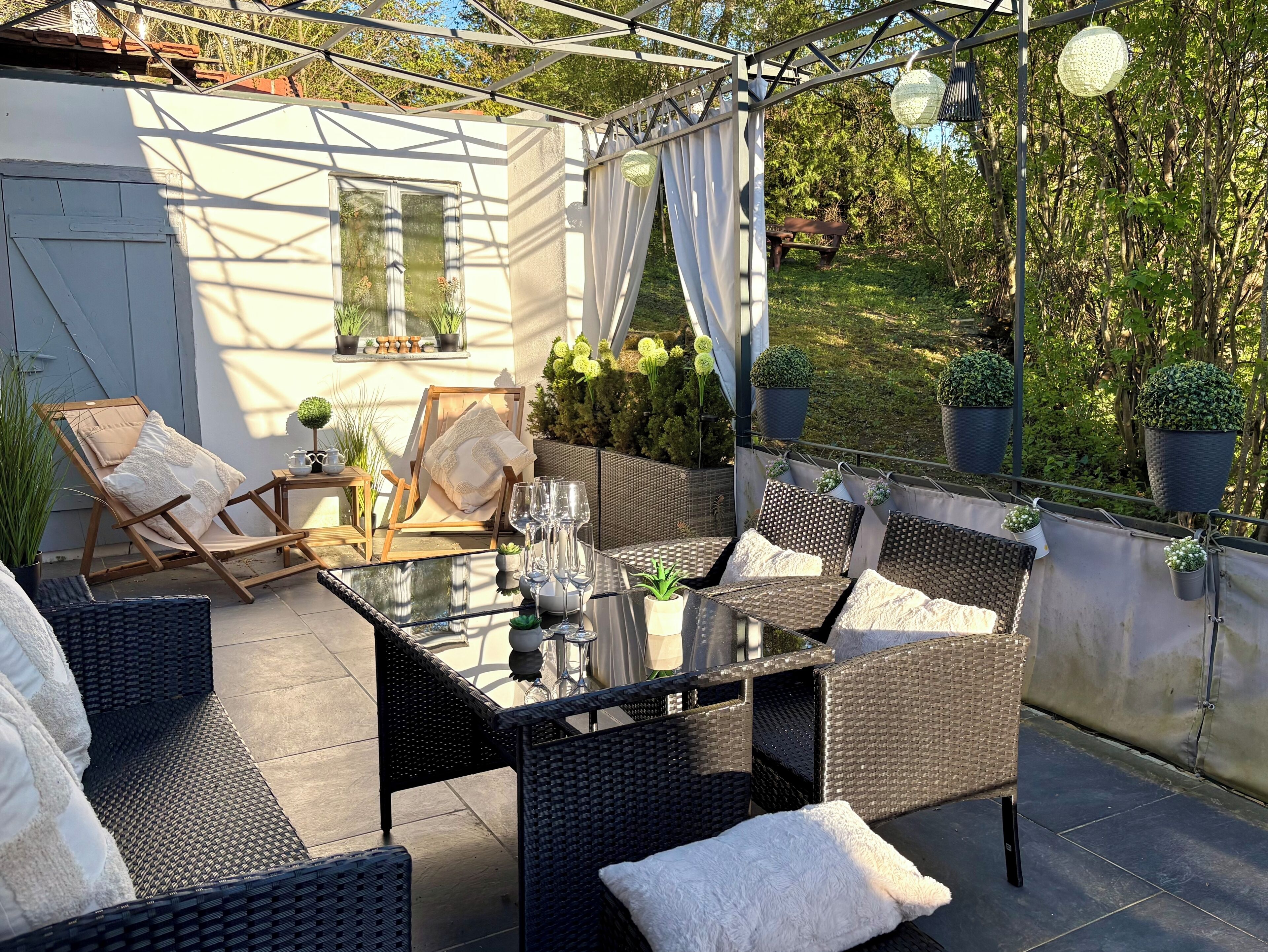 An outdoor patio with wicker furniture, a glass table, and potted plants.