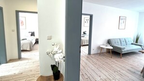 A modern living room with a grey sofa, a small round table, and a potted orchid. A bed with a white duvet and pillows is visible in the background. - AlbGlück 2, Hechingen, 1–7 people, castle 5 km away (Hechingen)