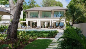 Uma casa de dois andares com piscina, área de estar externa e vegetação exuberante.