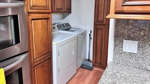 Une cuisine compacte dotée de meubles en bois, d’un four en acier inoxydable, d’un lave-linge et d’un plan de travail en granit.