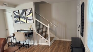 Un salon moderne avec un plancher en bois, un bureau avec une chaise, un escalier et une grande fenêtre avec des stores.