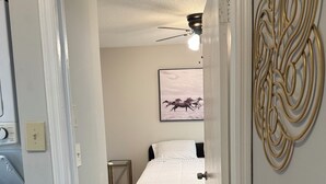 Une chambre à coucher avec un lit, un ventilateur de plafond, une lampe fixée au mur et un tableau encadré accroché au mur.