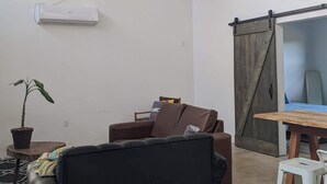 Ein geräumiges Zimmer mit einer schwarzen Couch, einem Holztisch, einer Schiebetür im Bauernhausstil und einem Topfpflanzen.