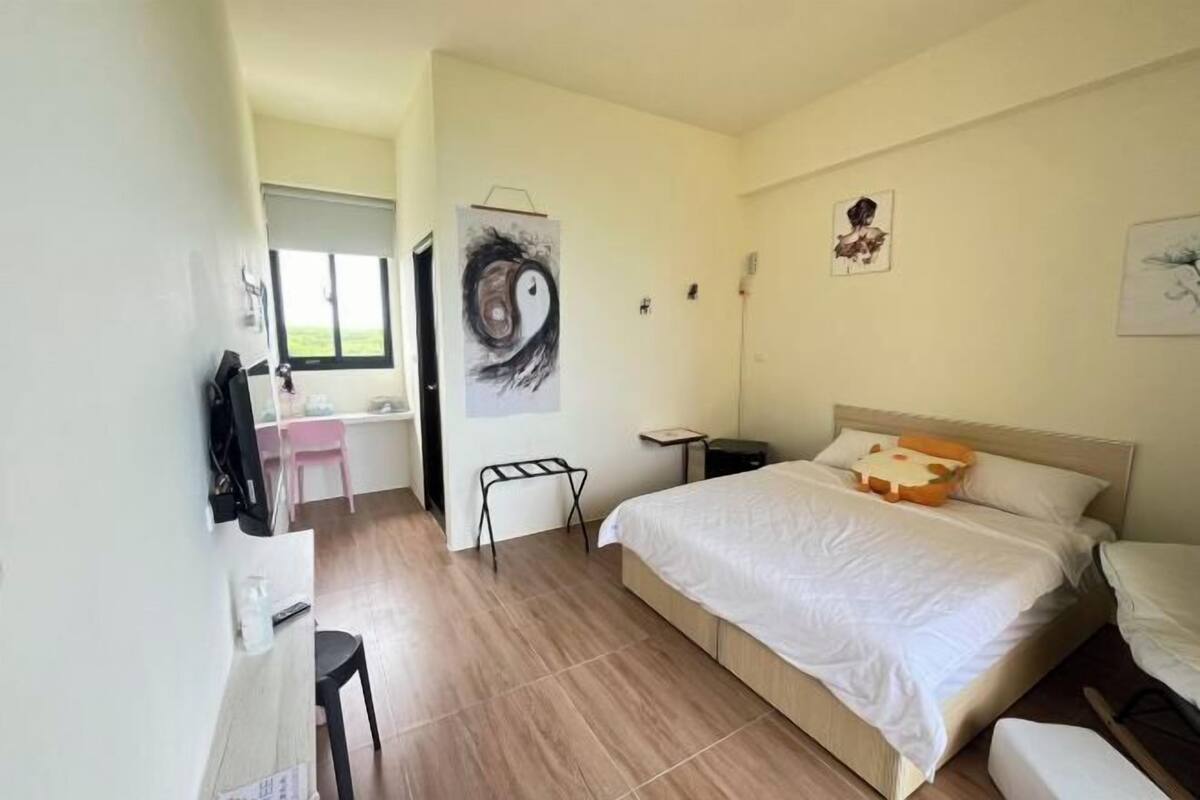 Una camera da letto con un letto, una scrivania, una sedia, una TV e opere d'arte alle pareti.