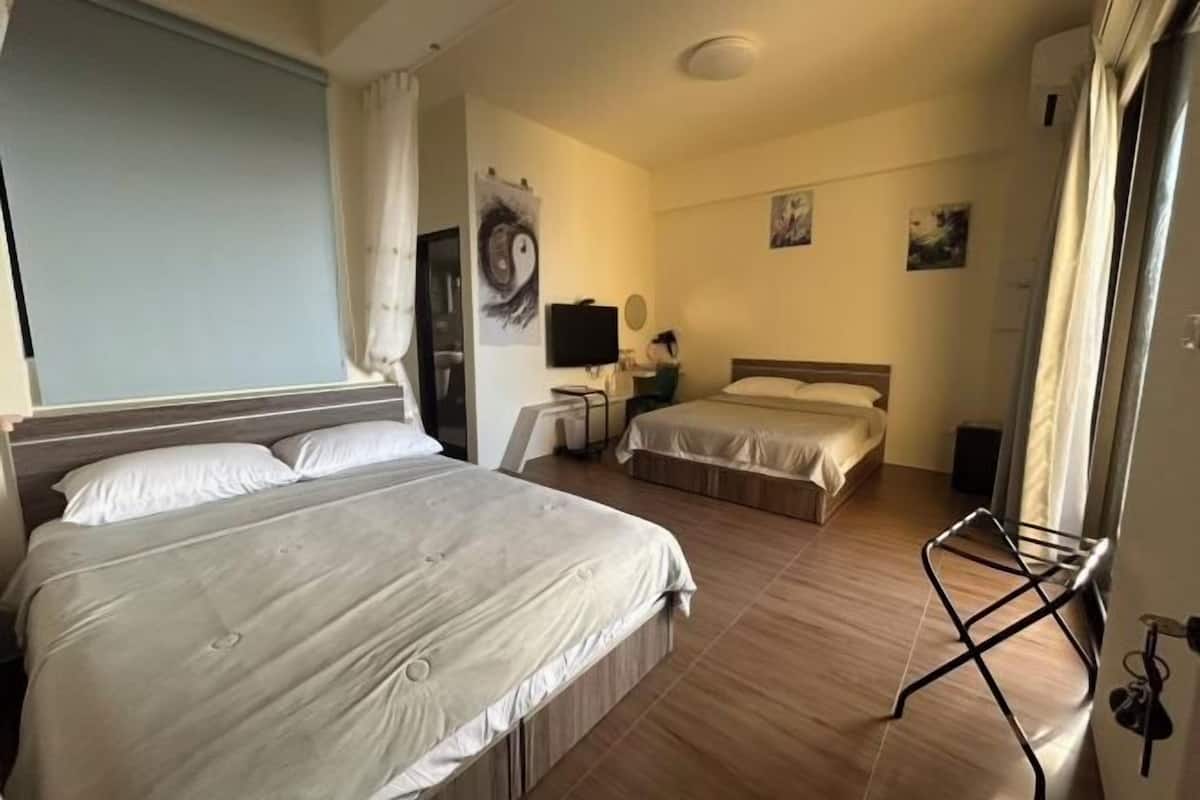 Una camera d'albergo con due letti, una televisione a schermo piatto, una scrivania e una finestra con tende.