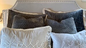 Une chambre à coucher avec un lit doté d’une tête de lit capitonnée, de plusieurs coussins ornés de motifs brodés et d’une œuvre d’art encadrée représentant un aigle, accrochée au mur.
