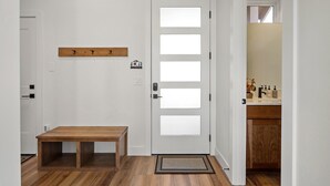 Un couloir avec un banc en bois, une porte blanche dotée de panneaux en verre dépoli et une petite étagère en bois au-dessus de la porte.