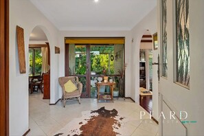 A spacious interior with a large glass door leading to a balcony, a wicker chair, a small table with a vase, and a cowhide rug.