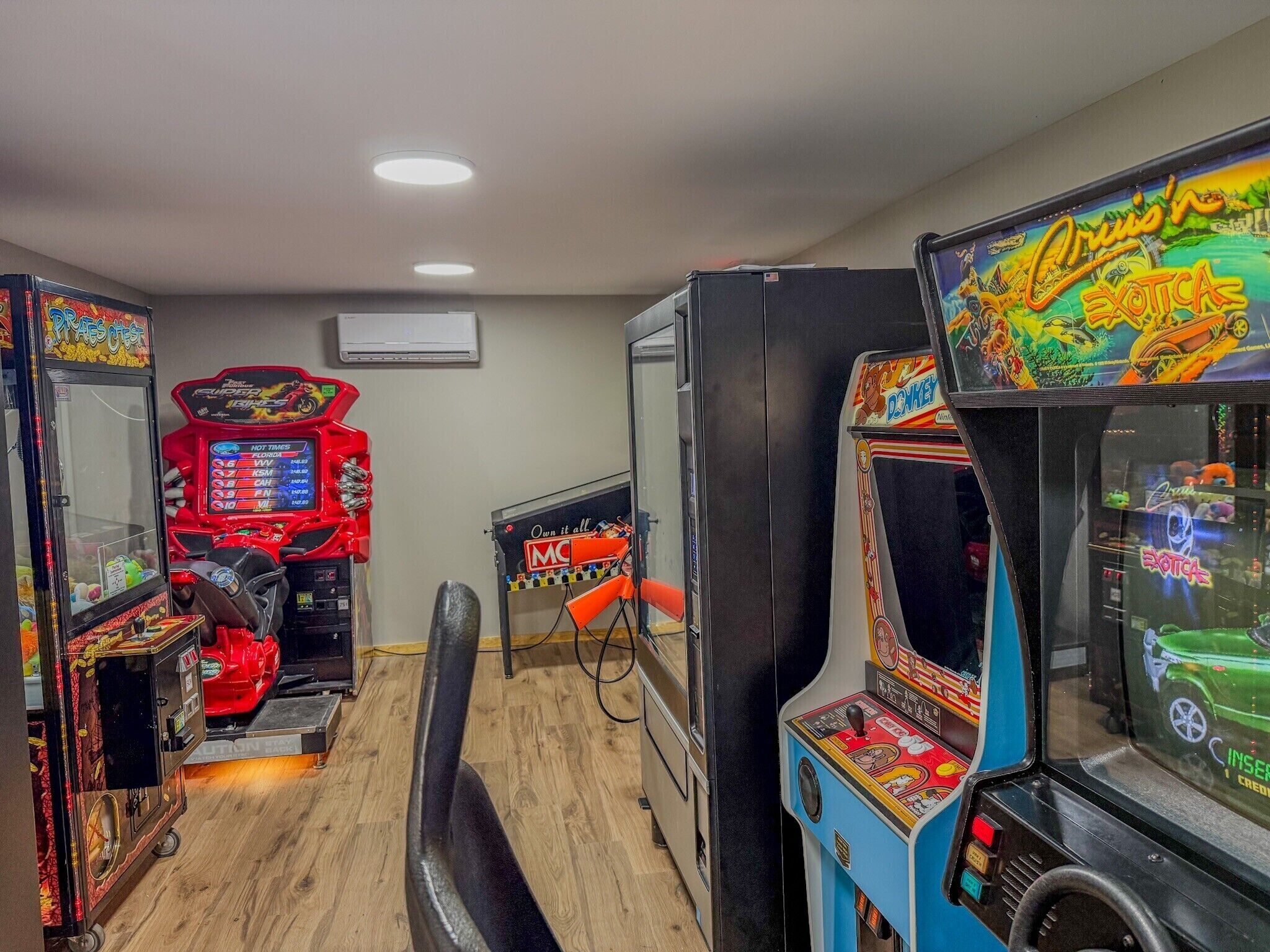 Une rangée de jeux d’arcade dans une pièce au plancher en bois et éclairée par un plafonnier.