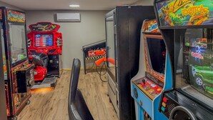A row of arcade games in a room with wooden flooring and a ceiling light. - Pine & Paddle | Family Cabin | Sleeps 7 (Hammond)