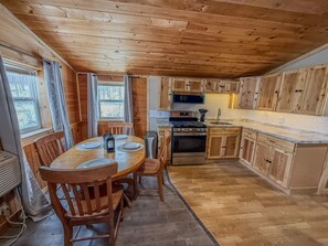 A wooden cabin interior with a dining table, chairs, a stove, oven, microwave, and wooden cabinets.