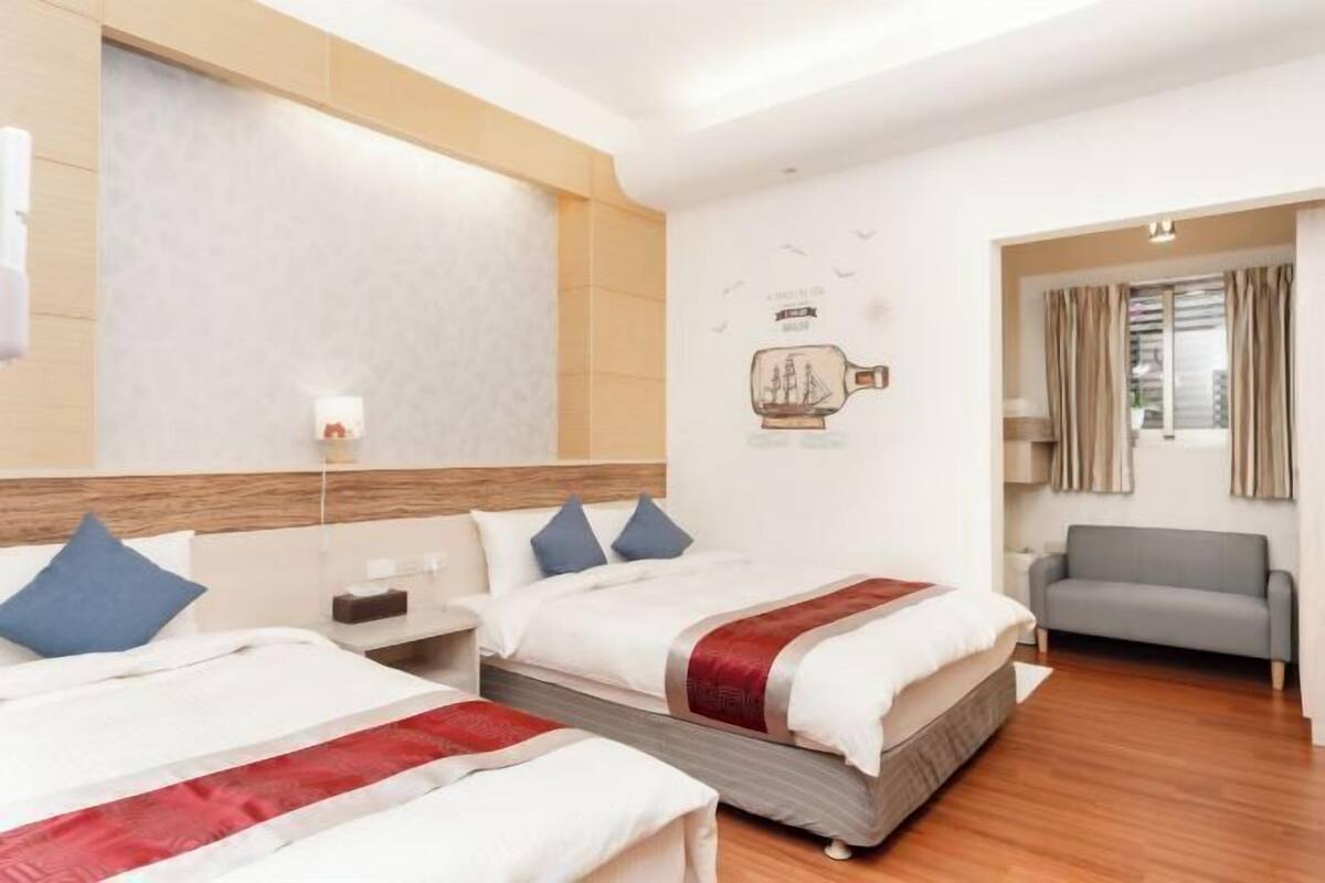 A hotel room with two beds, a sofa, a window with curtains, and a wall decoration.