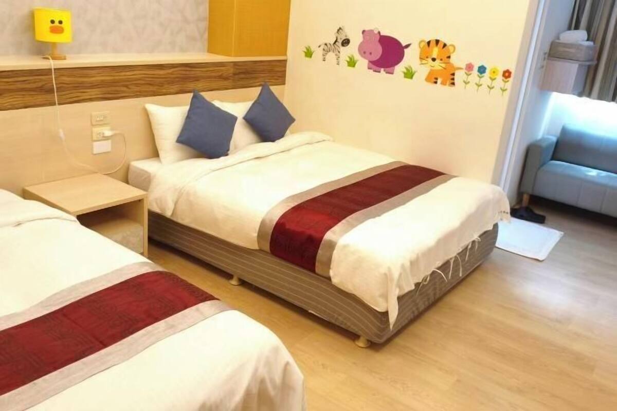 A hotel room with two beds, a wooden headboard, a wall with animal stickers, and a small table.