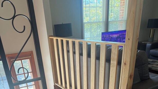 En trätrappa med ett räcke, en grå soffa och en tv-apparat i bakgrunden.