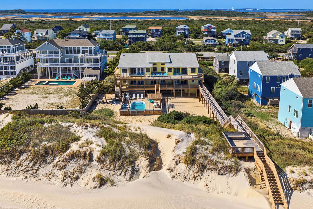 A beachfront property with multiple houses, a swimming pool, and a beach access walkway.