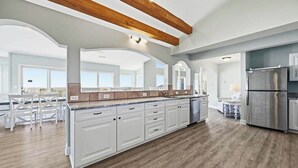 A spacious kitchen with white cabinetry, a large island, and a stainless steel refrigerator.