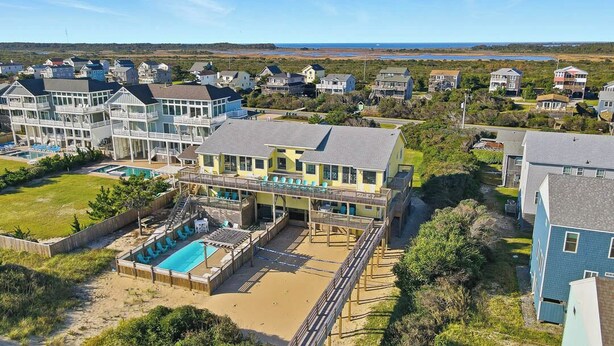A coastal residential area with a large house featuring a pool, a deck, and a view of the ocean.