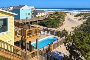 A beachfront property with a wooden deck, a swimming pool, and a view of the ocean. - Tide's a Wastin' | Oceanfront | Private Pool and Hot Tub (Nags Head)