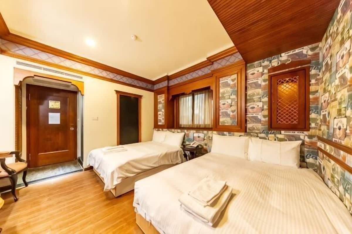 A hotel room with two beds, wooden flooring, a door, and a window with a decorative lattice.