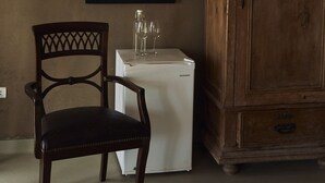Quarto com um armário de madeira, um quadro na parede, uma cadeira e um eletrodoméstico branco pequeno.