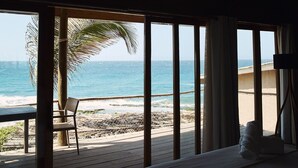 Quarto com cama grande, vista para a praia e uma palmeira.