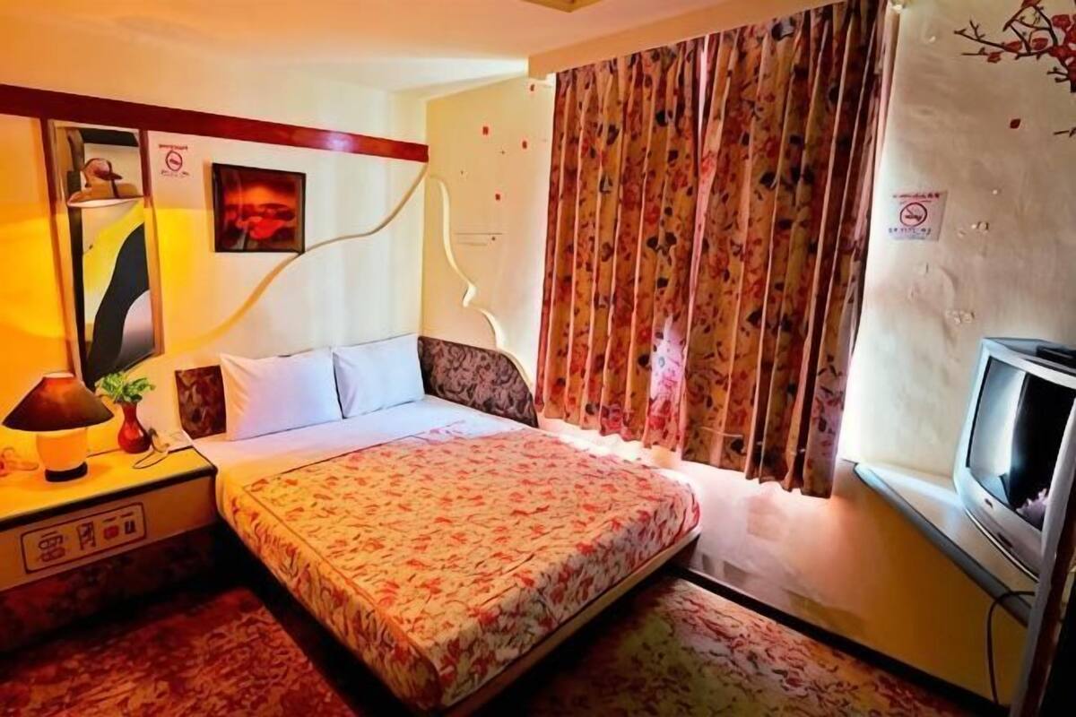 A hotel room with a bed, a TV, a nightstand, and a window with curtains.