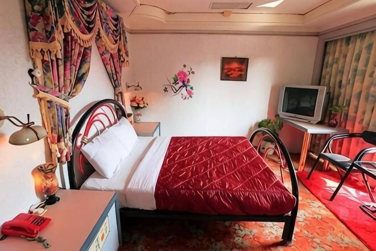 A hotel room with a bed, a desk, a chair, a TV, and a window.