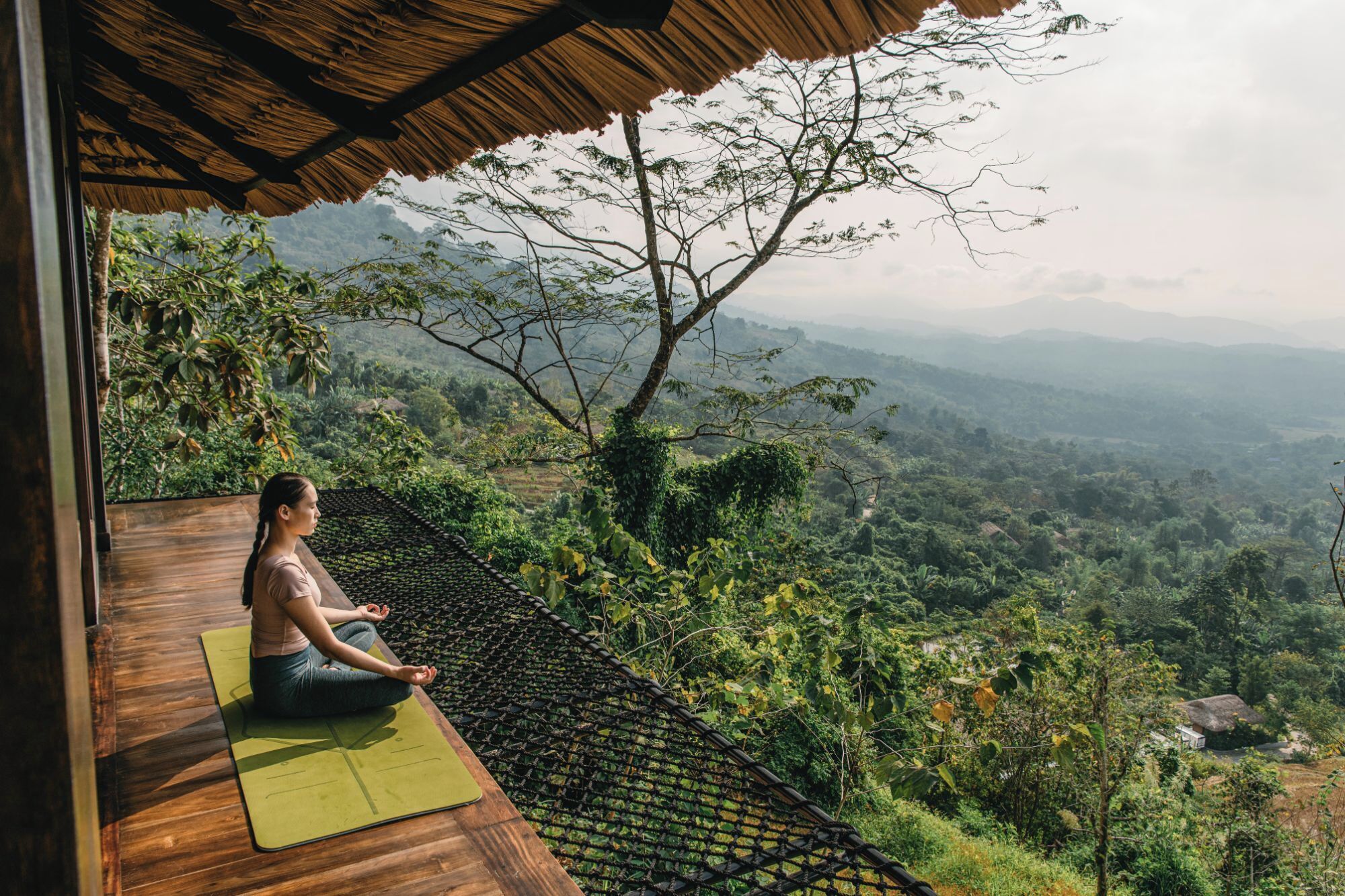 A person meditating on a wooden deck with a view of a lush valley.