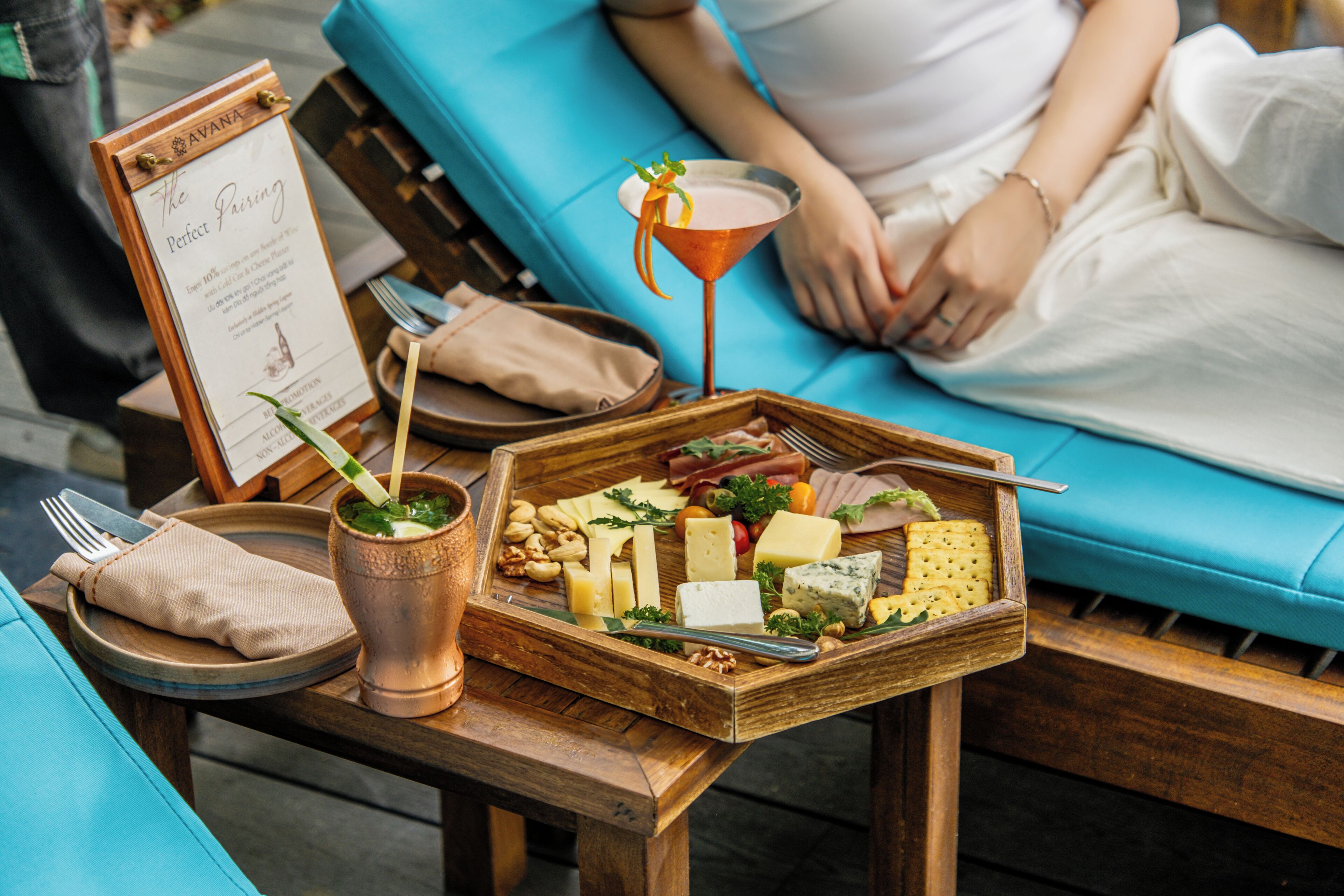 Una bandeja de madera con queso, nueces y una copa de martini sobre una mesa.