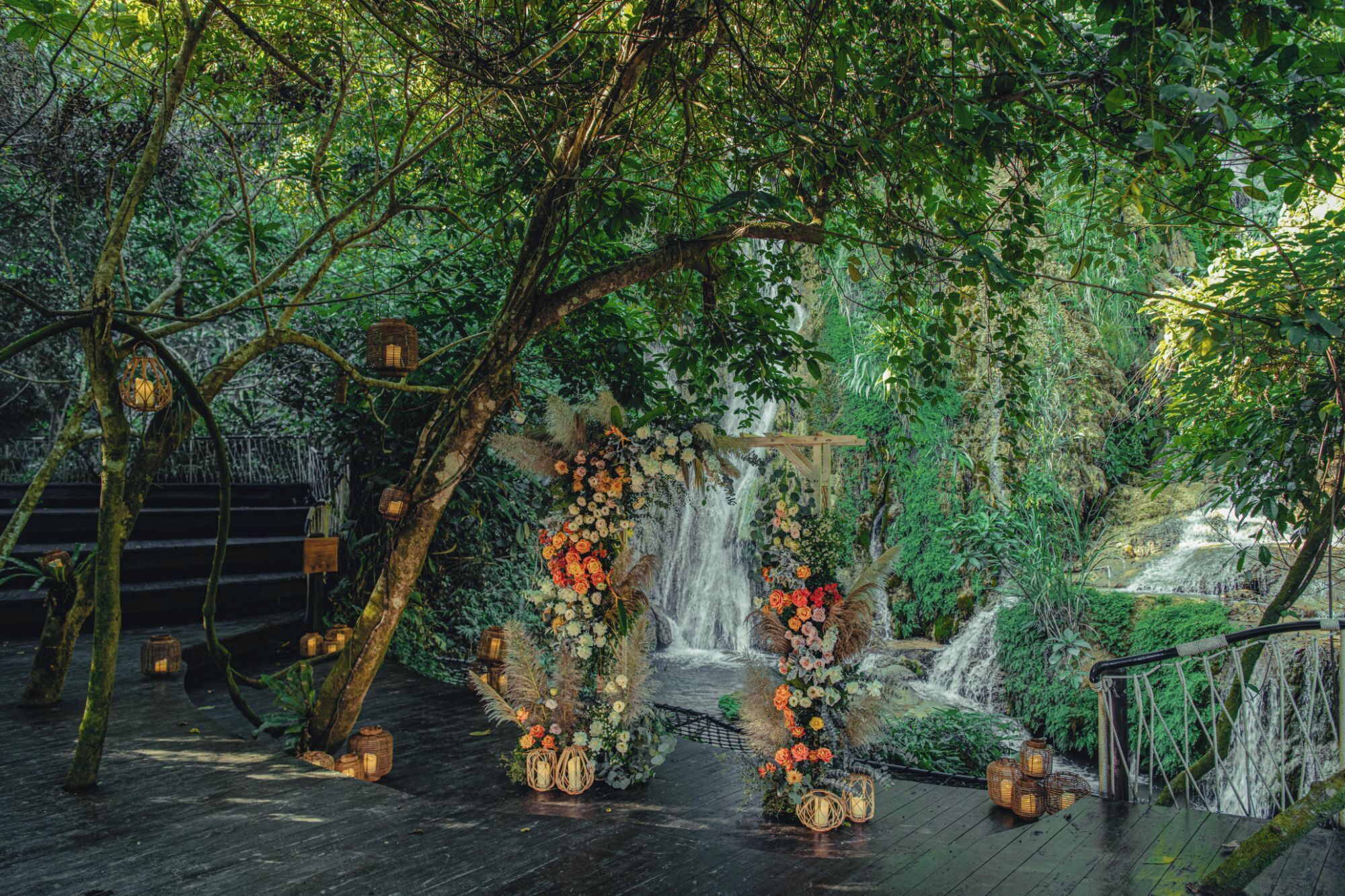 Una terraza de madera con un arco floral que da a una cascada.