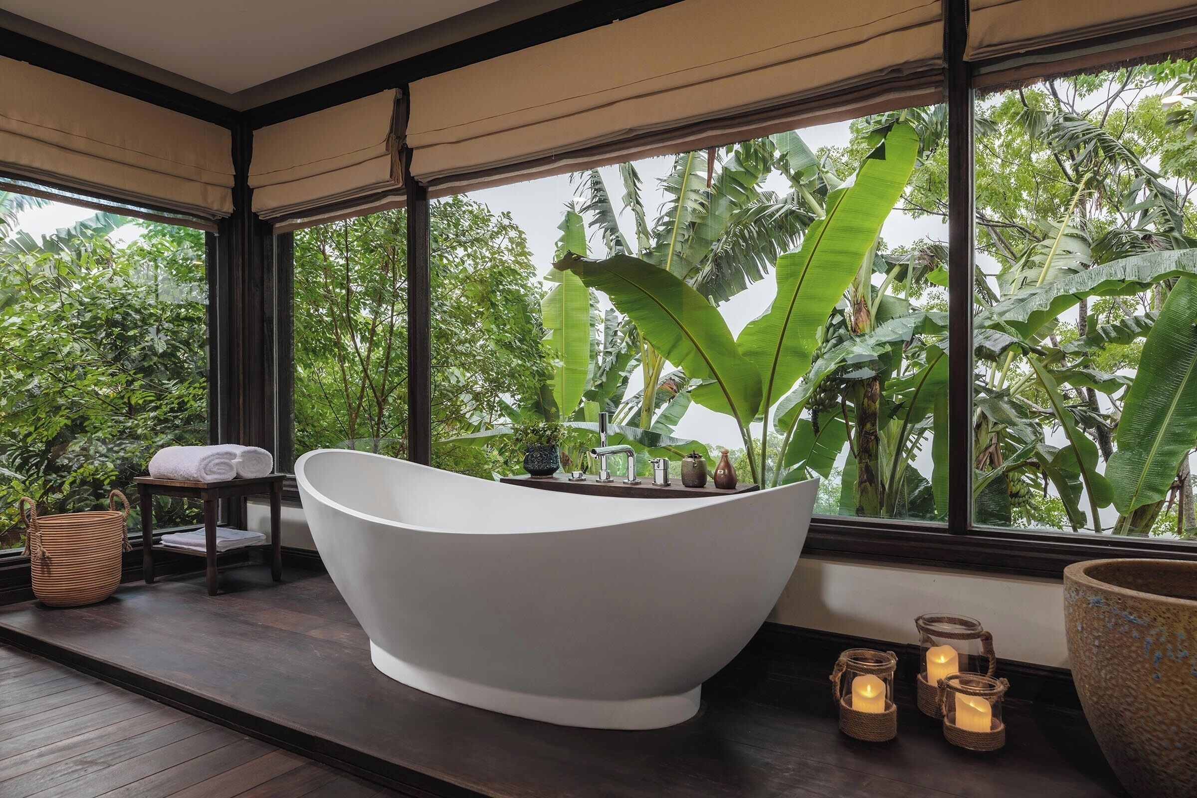 A modern bathroom with a freestanding bathtub, a window with a view of lush greenery, and a small table with towels.