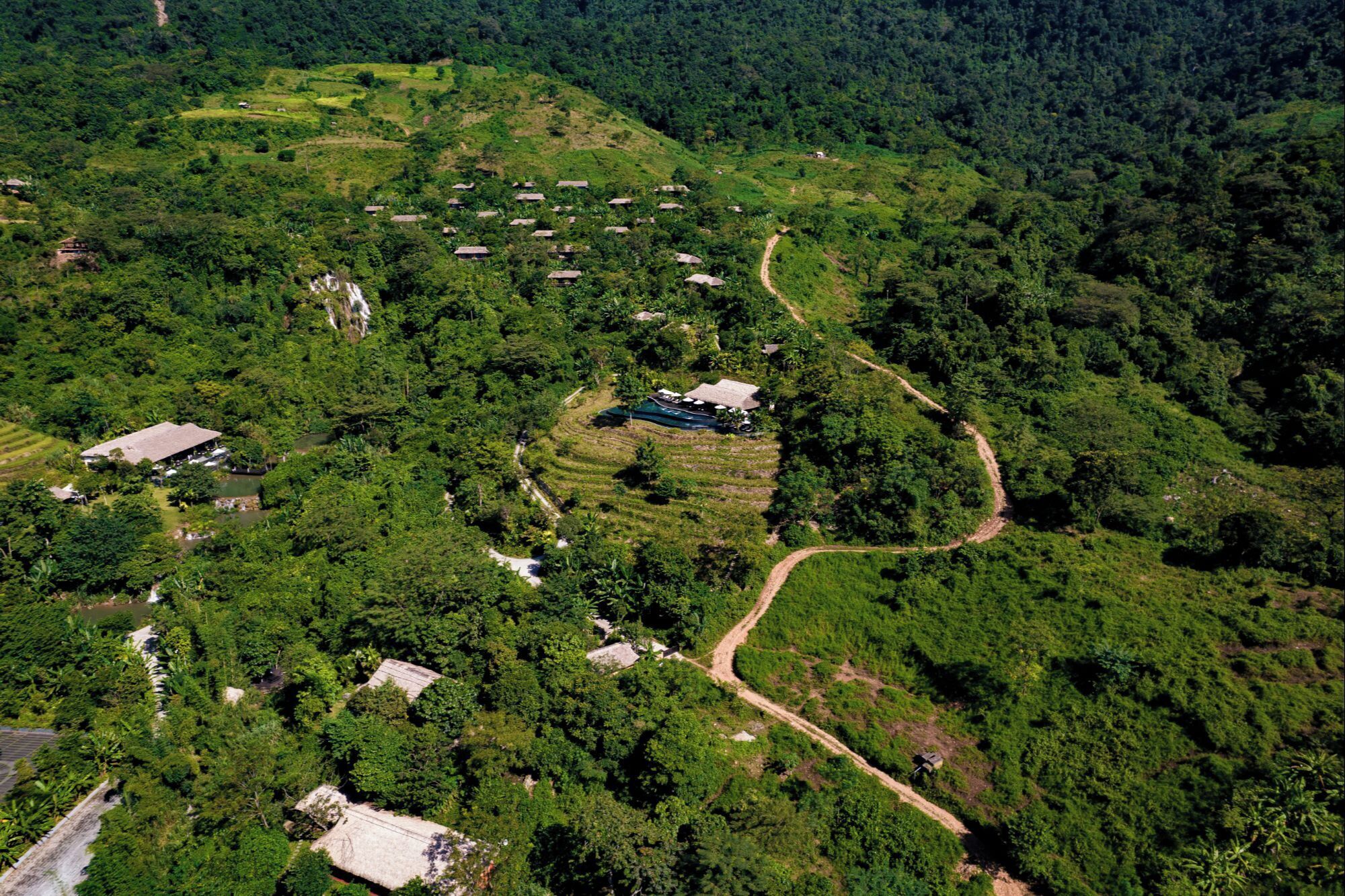 Vista aérea de una zona rural con campos en terrazas, casas dispersas y un sendero sinuoso.