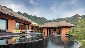 A resort with a infinity pool, thatched-roof structures, and a mountainous backdrop. - Avana Retreat (Bao La)