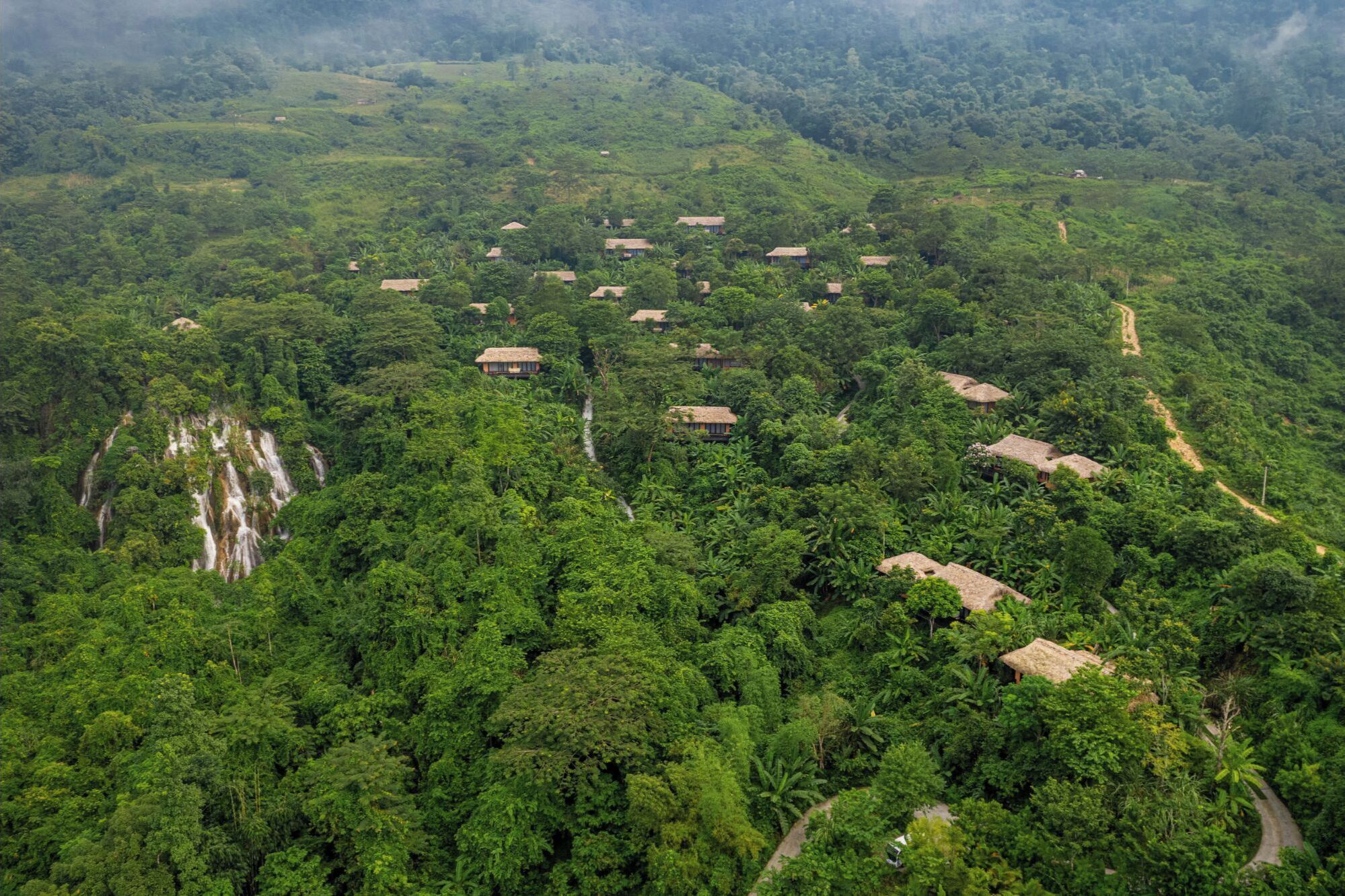 Un paisaje exuberante y verde con varias cabañas de techo de paja dispersas en un terreno ondulado.