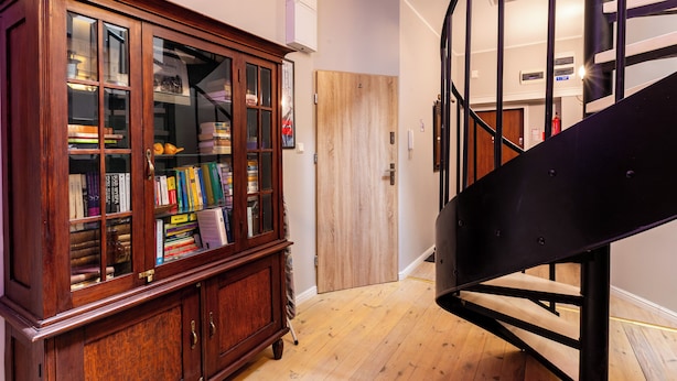 Ein Bücherregal aus Holz mit Büchern, eine Holztür und eine schwarze Wendeltreppe.