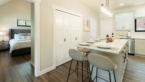 A modern kitchen with white cabinetry, a central island with bar stools, and a dining area with a table set for two. - Walk to Main Street & Town Lift, Private Hot Tub, Garage Parking, On Shuttle Route (Park City)