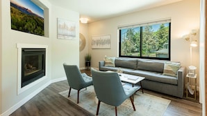 A living room with a fireplace, a sofa, two chairs, a coffee table, and a large window with a view of trees. - Walk to Main Street & Town Lift, Private Hot Tub, Garage Parking, On Shuttle Route (Park City)