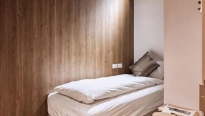 A single bed with pillows, a wooden wall, and a small bedside table with a remote control. - Twin Star Inn (Taipei)