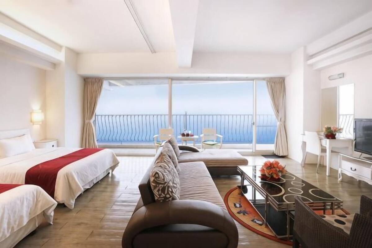 Ein Hotelzimmer mit Balkon, einer Couch, einem Bett, einem Fernseher und einer Essecke.