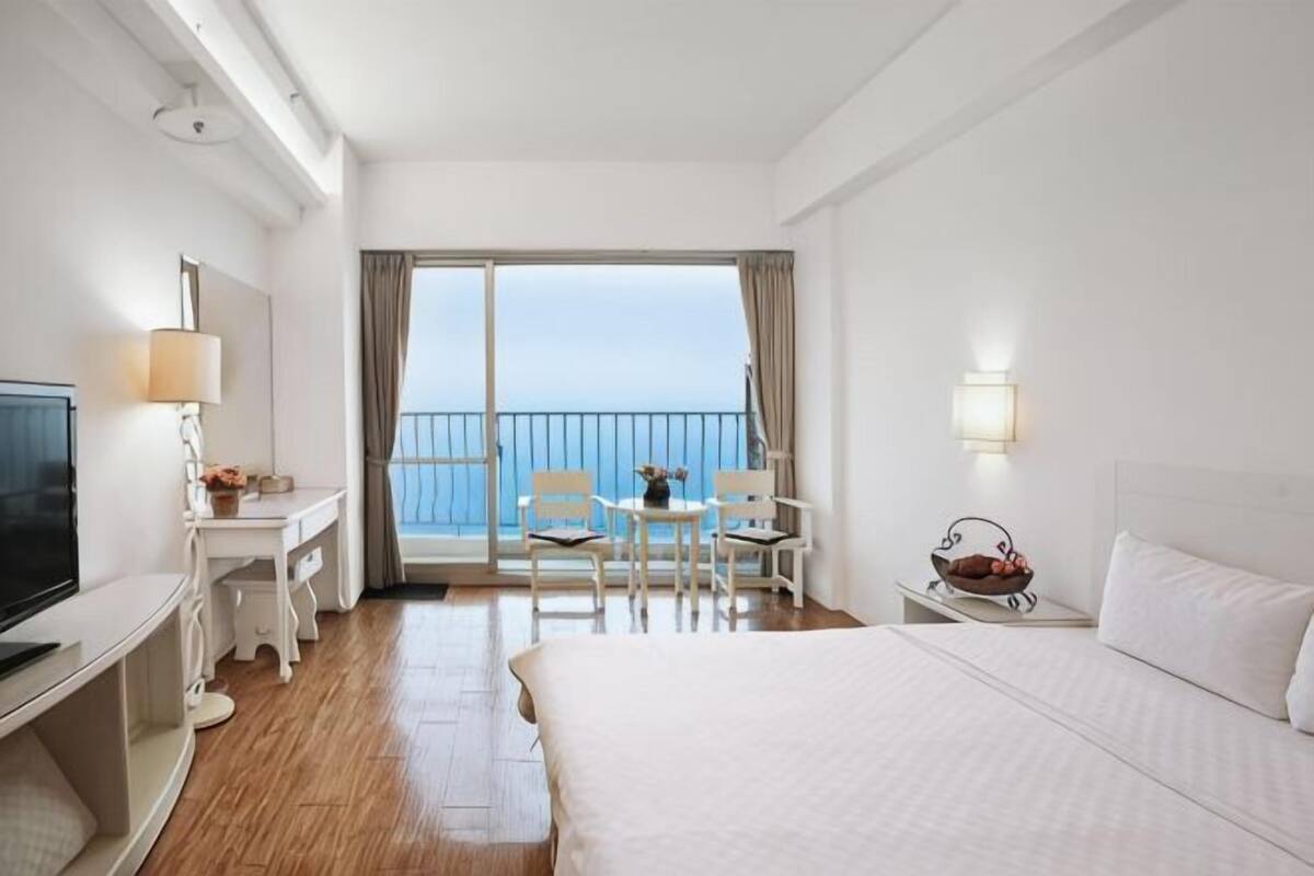 Ein Hotelzimmer mit Bett, Schreibtisch mit Fernseher, Stuhl, Tisch und einem Balkon mit Aussicht.