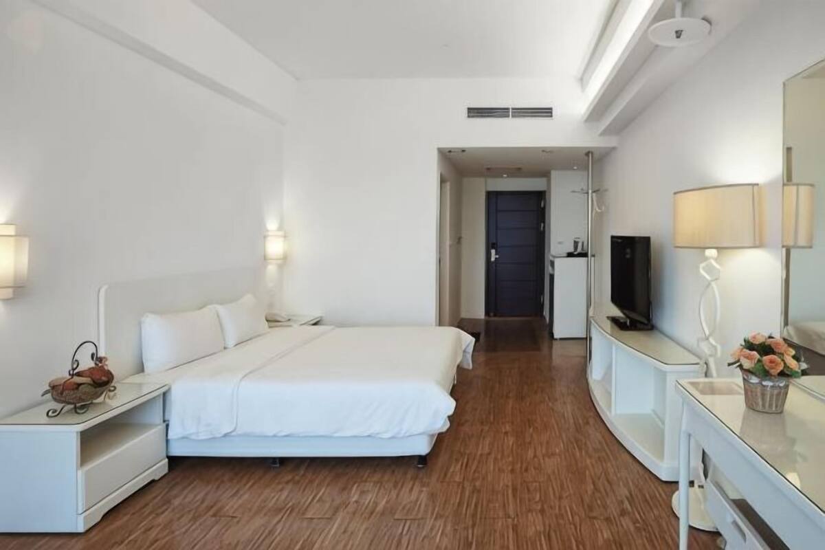 Ein Hotelzimmer mit einem großen Bett, Nachttischen, einem Schreibtisch, einem Sessel, einem Fernseher und einem Spiegel.