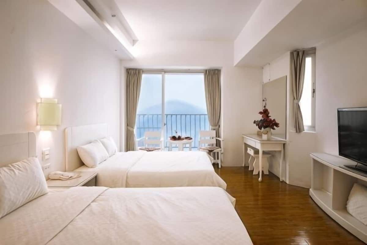 Ein Hotelzimmer mit zwei Betten, einem Schreibtisch, einem Stuhl, einem Fernseher und einem Balkon mit Blick.