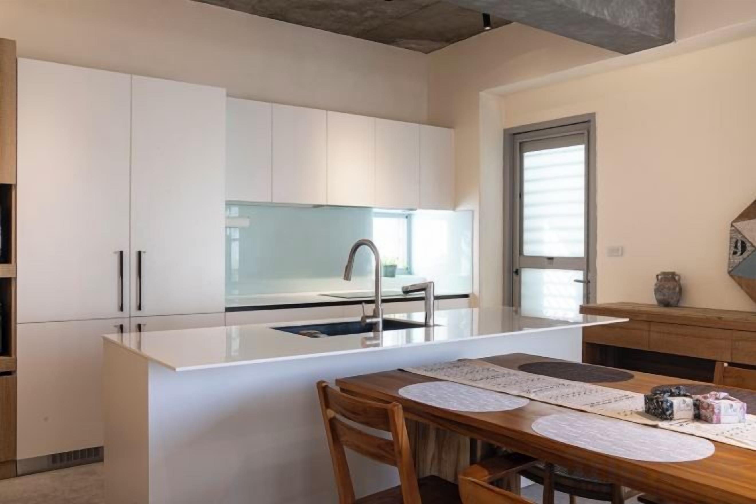 A modern kitchen with white cabinetry, a central island, and a dining area with a wooden table and chairs.
