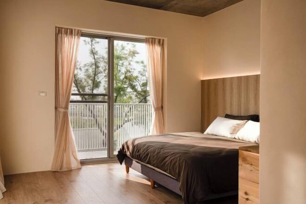 A bedroom with a bed, a wooden dresser, and a balcony with curtains.