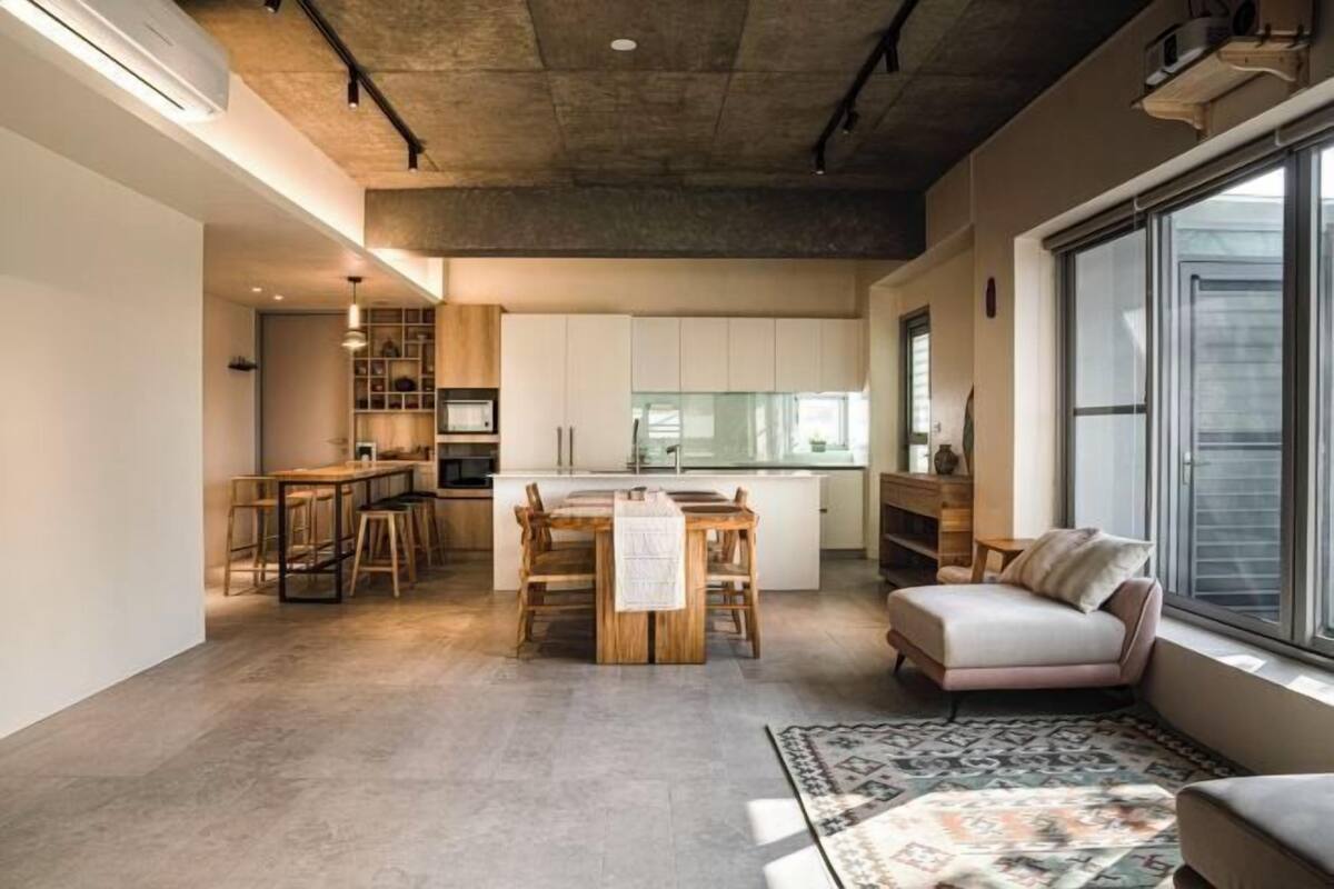 A modern kitchen with white cabinets, a dining area with a wooden table and chairs, and a large window providing natural light.