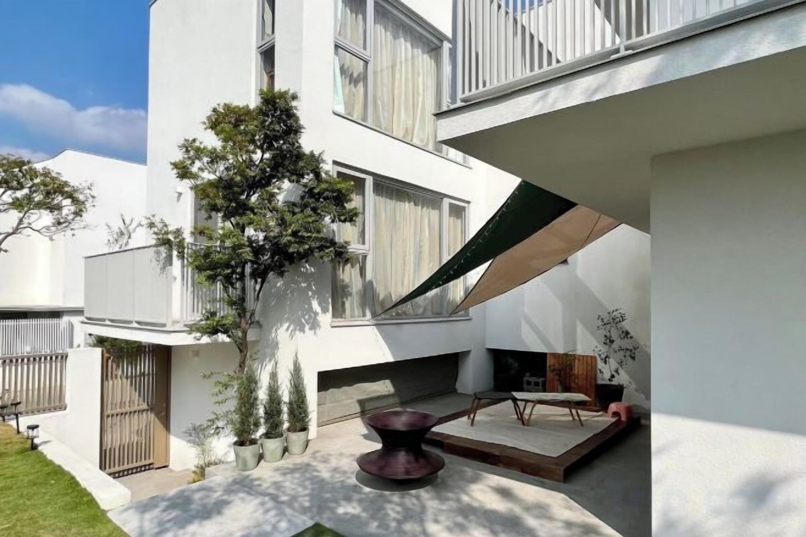 A modern building with a flat roof, a small garden area with a tree, and a seating area with a table and chairs.